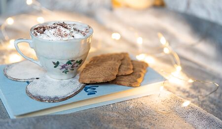 Hot chocolate and cookies laying on book in bed with lights, cozy winter conceptの写真素材