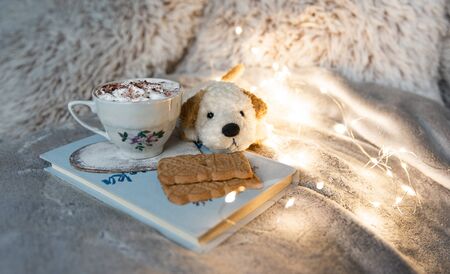 Coziness and comfort in winter concept, hot chocolate and cookies with plush toy in warm bedの写真素材