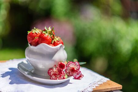 Jug full of strawberries with flower decoration, summer dining in gardenの写真素材