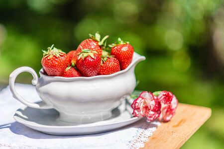 Jug full of strawberries with flower decoration, summer dining in gardenの写真素材