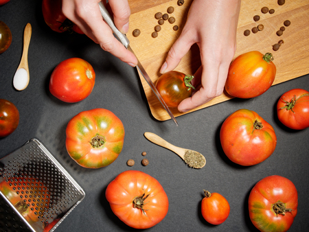Hand of a young woman cutting fresh tomato. Top view, flat lay.の写真素材
