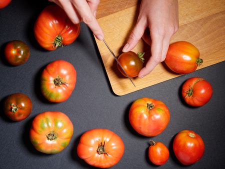 Hand of a young woman cutting fresh tomato. Top view, flat lay.の写真素材