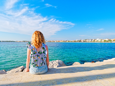 The woman sits and looks at the sea and the city. Alghero.の写真素材