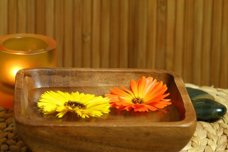 Two marigolds - yellow and orange, floating on woter in wooden bowl. Therapeutic calming spa treatmentの写真素材