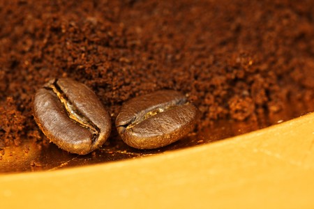 Two arabic coffee beans on ground coffee on golden plateの写真素材