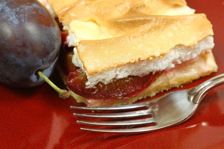 Closeup of the plum cake with freah plum and fork on red plate. Autumn cake with meringueの写真素材