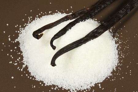 Vanilla beans and crystal sugar on brown background