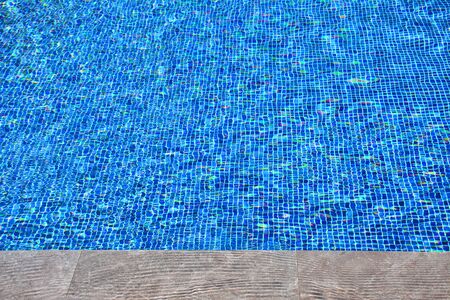Clear water in blue tiled swimming pool. View with the edge