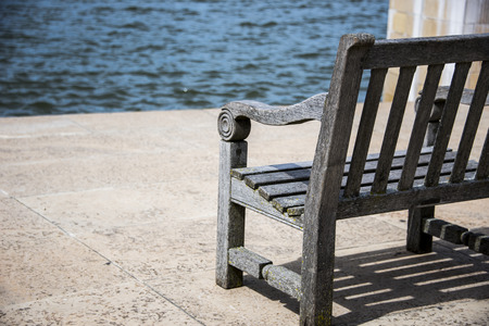 Empty bench facing towards beautiful blue water with sunlight hitting directly on the whole area.の写真素材