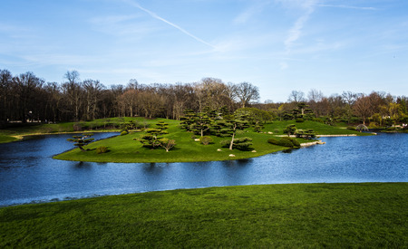 Small lake flowing through garden, hillside with trees and bushes growing.の写真素材