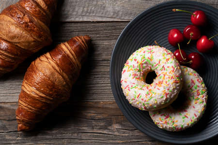 Freshly baked french croissant and colorful glazed donuts exposed on the decorative platter with...