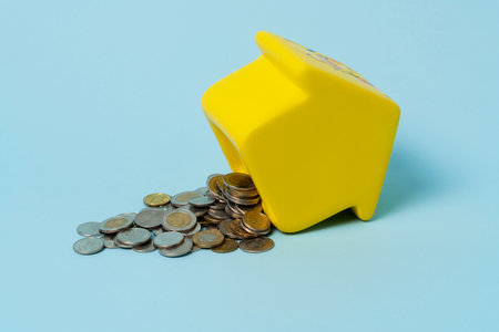 Yellow piggy bank with with a lot of coins scattered all over the blue background