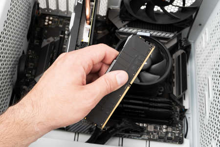 Hands of computer engineer instaliing RAM into modern