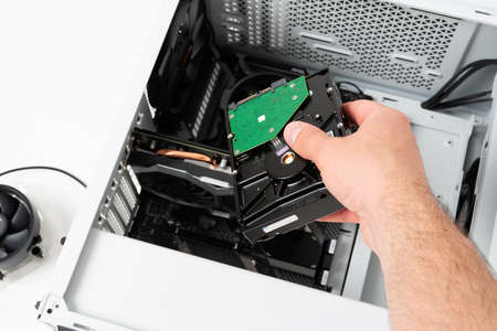 Hands of computer engineer instaliing hard drive into modern