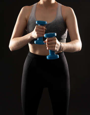 Close up photo of fit woman working out with dumbbells on the black background