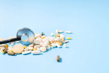 Top view of black stethoscope and colorfull pills scattered all over the blue backgroundの写真素材