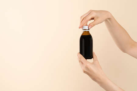Image of hands holding a brown bottle of liquid cold medication. Bottle without label for product placement or product presentation. beige background.の写真素材
