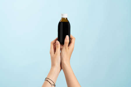 Image of hands holding a brown bottle of liquid cold medication. Bottle without label for product placement or product presentation. blue background.の写真素材
