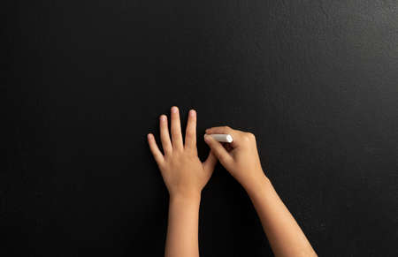 Image of little boy, s hands drawing picuters on the black chalk board.の写真素材