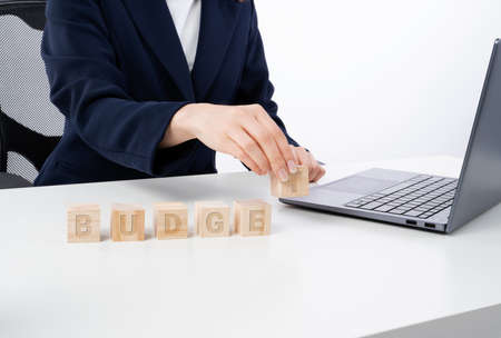 Young caucasian bussines woman stacking wooden blocks in her work office. Office interior, laptop, notebook and flower on white desk.の写真素材