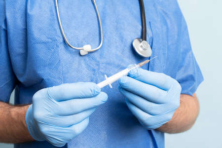 Close up picture of male doctor wearing medical scrubs and stethoskope over neck showing syringe full of vaccination.の写真素材