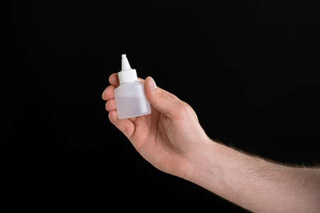 A close up image of man's hand holding a bottle of glue isolated on black backgroundの写真素材