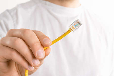 Man's hand holds yellow cable on white background. He is trying to connect computer to the internet instead of a wifi connectionの写真素材
