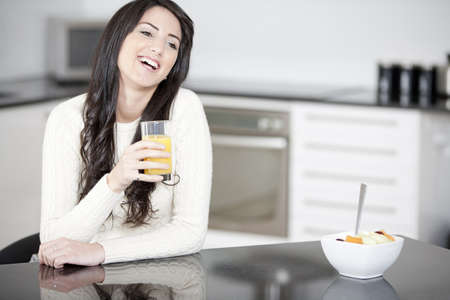 Young woman in kitchen enjoying some orange juice and fresh fruitの写真素材