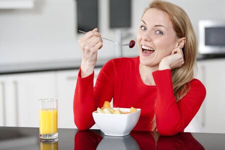 Young woman enjoying a bowl of fresh fruit in her kitchen with orange juiceの写真素材