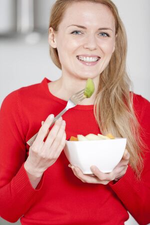 Young woman enjoying a bowl of fresh fruit in her kitchenの写真素材