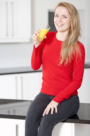 Young woman sitting on counter drinking orange juiceの写真素材