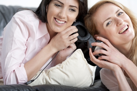 Two young woman listening to music on headphones at home.の写真素材