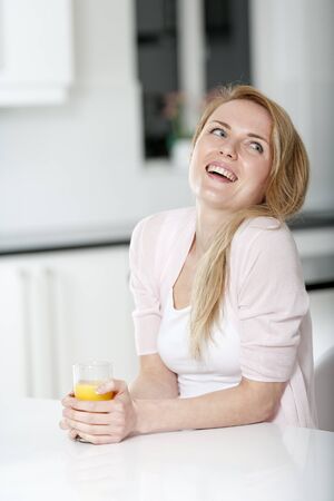 Young woman in pink shirt sitting at dining table at home with orange juiceの写真素材