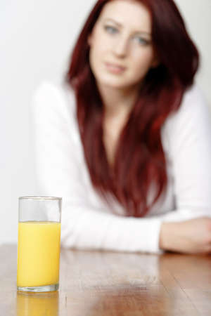 Glass of Orange juice with a female sitting in the background leaning on a tableの写真素材