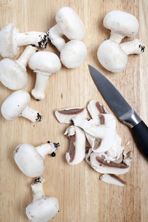 Fresh organic mushrooms being sliced on a wooden chopping boardの写真素材