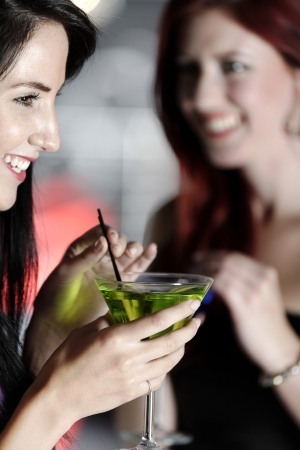 Two beautiful young woman chatting and drinking cocktails at a nightclub or wine bar.の写真素材