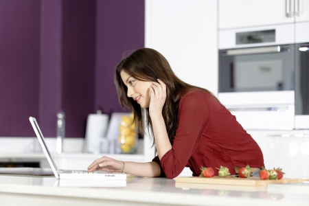Beautiful young woman reading a recipe from a laptop in her kitchenの写真素材