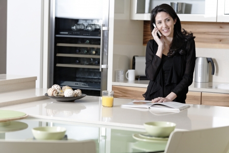 Attractive young woman talking on the phone in her kitchenの写真素材