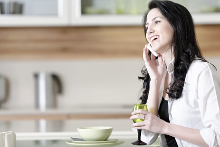 Beautiful young woman chatting on her mobile phone in her kitchenの写真素材