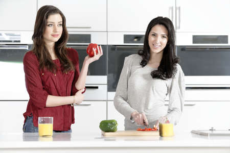 Two attractive young women preparing food in a white kitchen while talking.の写真素材