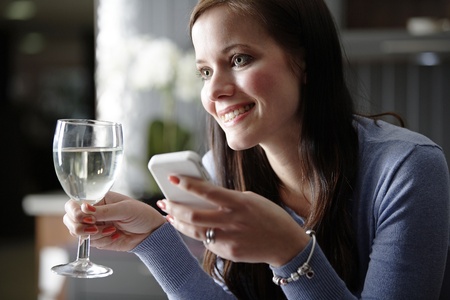 Attractive young woman enjoying a glass of wine in her kitchen while chatting on the phone.の写真素材