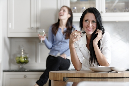 Two attractive young friends laughing and drinking wine in their kitchen.の写真素材