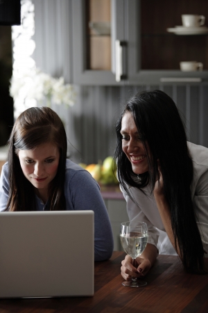 Two attractive friends looking at recipes on a laptop in their kitchen.の写真素材