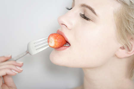 Beautiful young woman's face eating a strawberry.