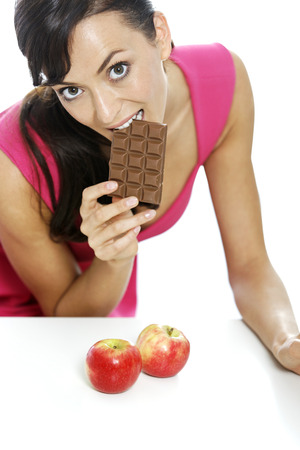 Young woman torn between a chocolate bar and fresh appleの写真素材