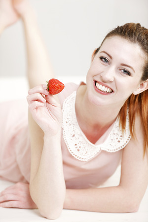 Beautiful young woman enjoying a fresh strawberry.の写真素材