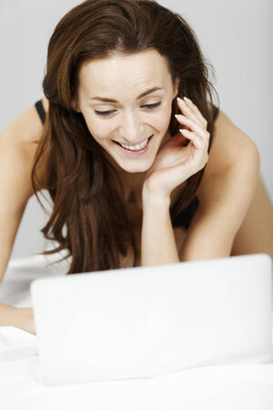 Beautiful young woman in black underwear using her laptop in bedの写真素材