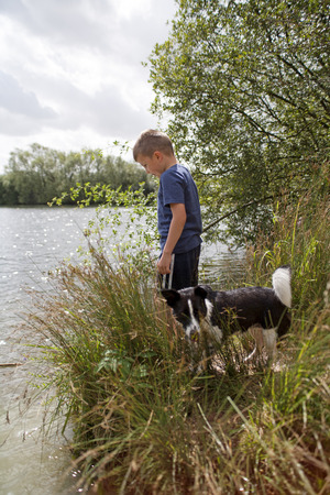 Young boy and his dog playing on the side of a lakeの写真素材