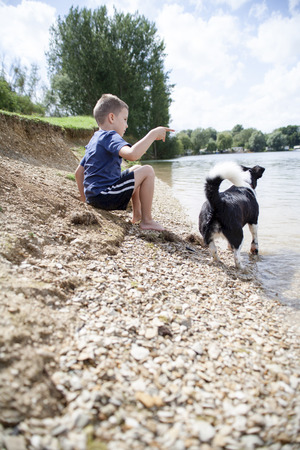 Young boy and his dog playing on the side of a lakeの写真素材