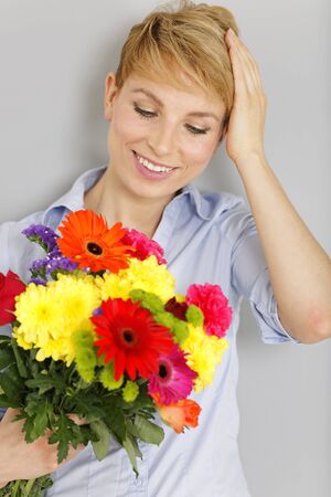 Beautiful young woman smiling and holding a fresh bouquet of colourful flowersの写真素材